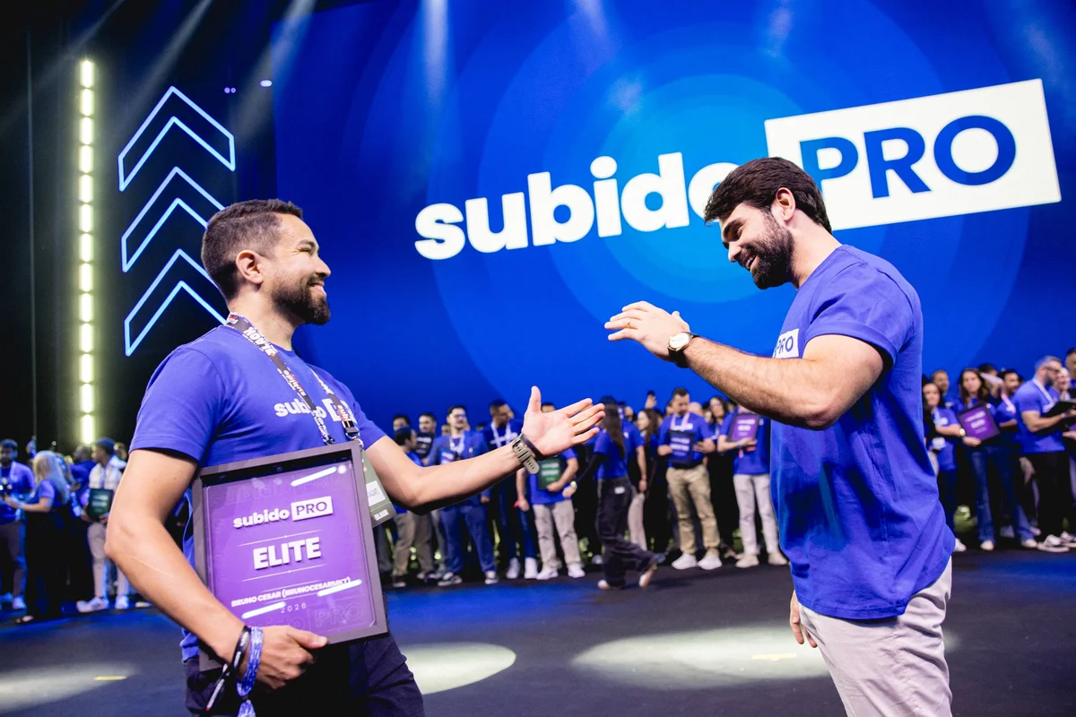 Bruno César em um evento da Subido, recebendo uma placa e cumprimentando outro participante no palco.
